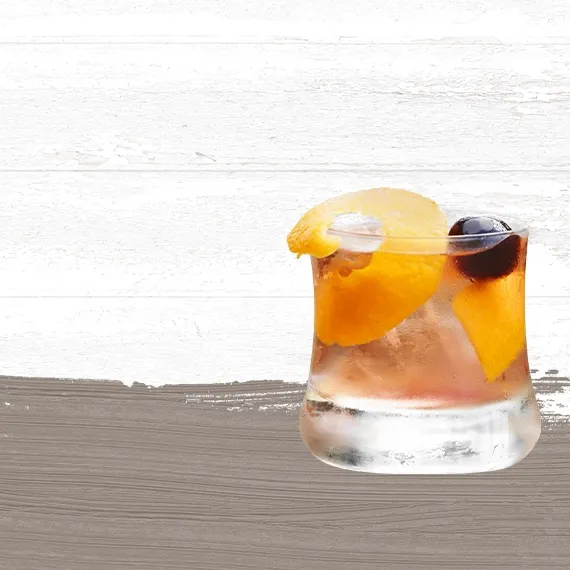 Cruzan® Morning cocktail, a light rum drink, in a rocks glass garnished with an orange peel and a black cherry set against a whitewashed background with a taupe paint swash.