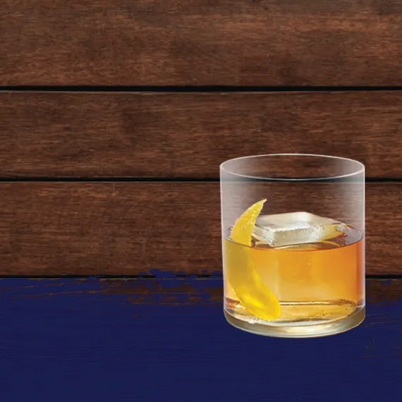 The Cruzan rum old fashioned dark rum cocktail is set against darker oak barrel panels in the background with a blue paint swash.