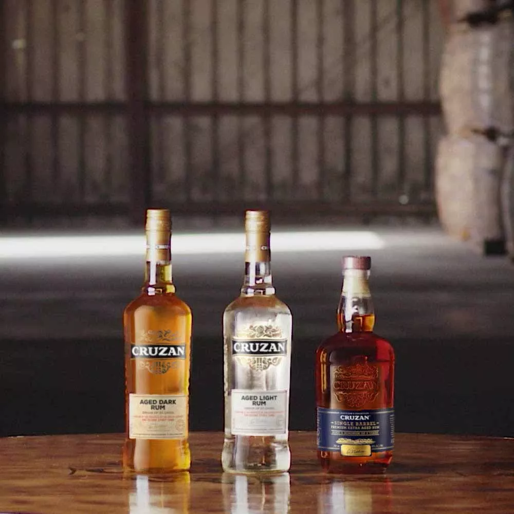 Image of Cruzan Aged Dark Rum, Cruzan Aged Light Rum and Cruzan Single Barrel Rum bottles on a wooden table.